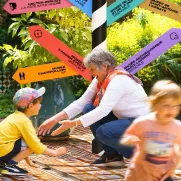 une grand mère et ses petits enfants jouant dans un jardin devant l'arbre des musées