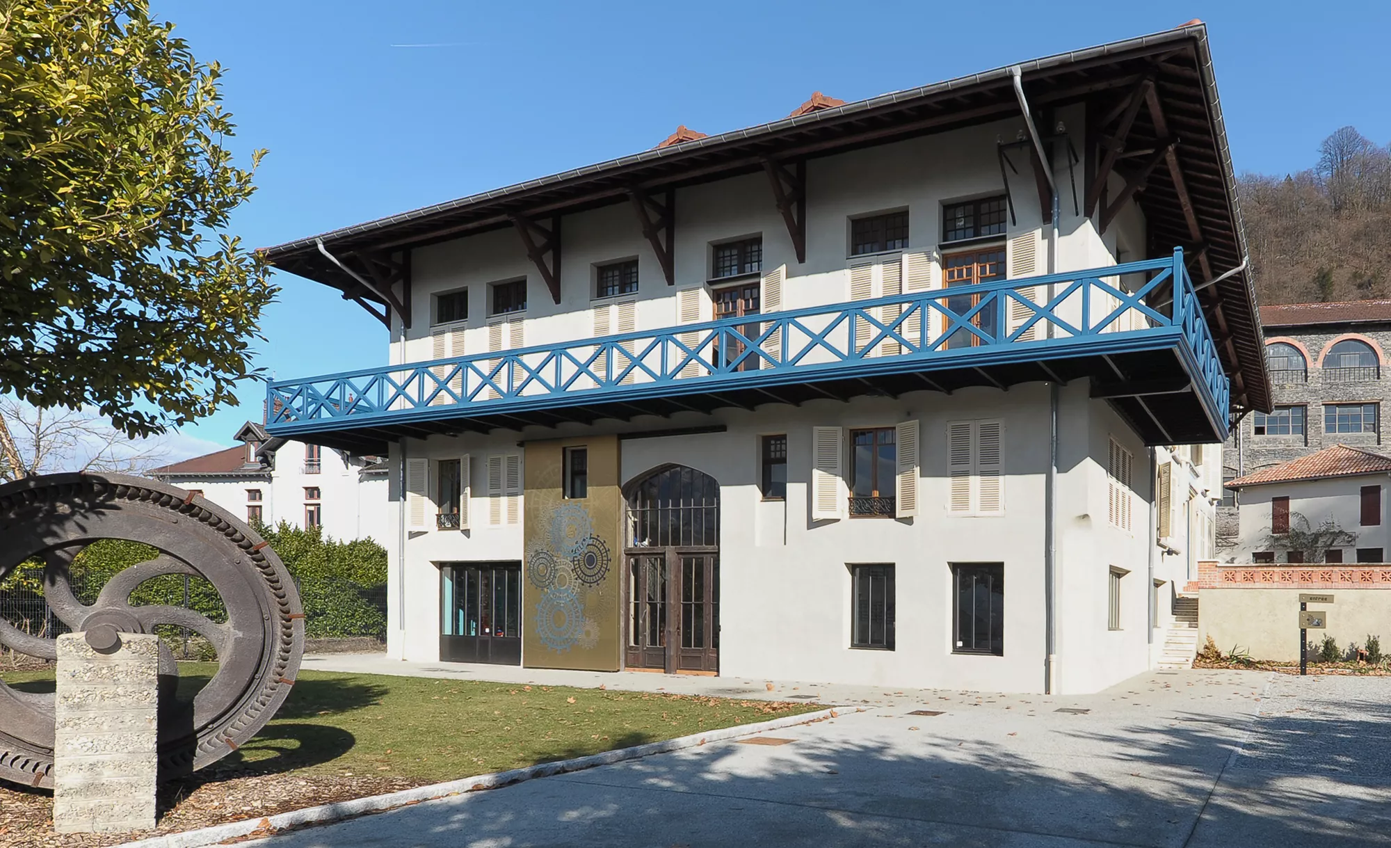 La Maison Bergès, façade ouest et l'une des turbines historiques présentées dans le parc Maison Bergès à Lancey, au premier plan une des turbines autrefois installée dans la papeterie Bergès et à l'arrière-plan l'ancien laboratoire de l'usine