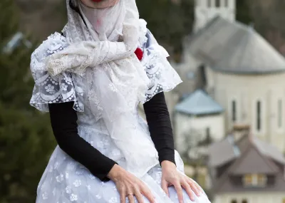 Photographie d'un personnage du Turak Théâtre masqué portant une robe de mariée devant l'église Saint Hugues © Raphael Licandro