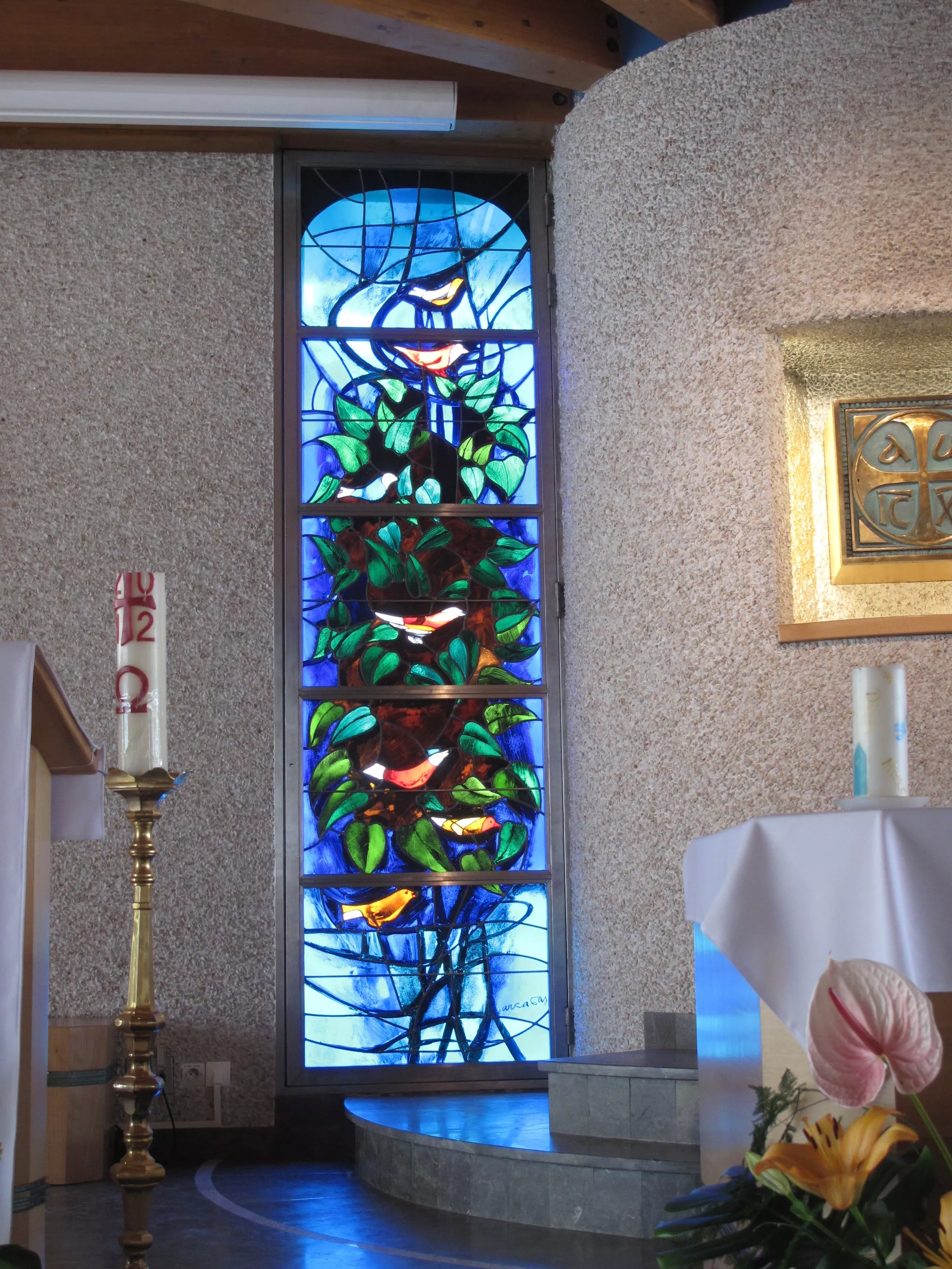 Vitrail bleu avec un buisson vert au milieu. Plusieurs oiseaux sont posés sur le buisson.