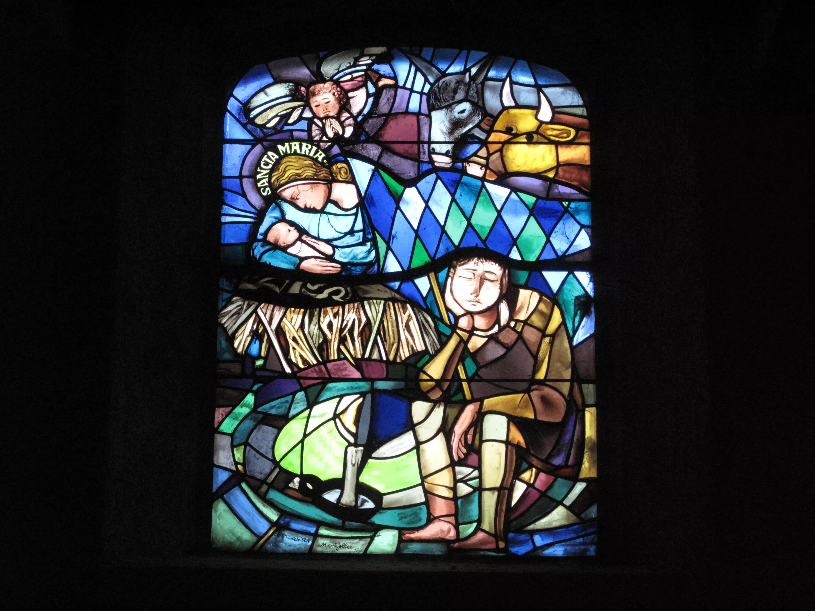 Joseph est au premier plan, assis. Au second plan, Marie est couchée dans un lit de paille. L'enfant Jésus vient de naitre, il est blotti contre Marie.