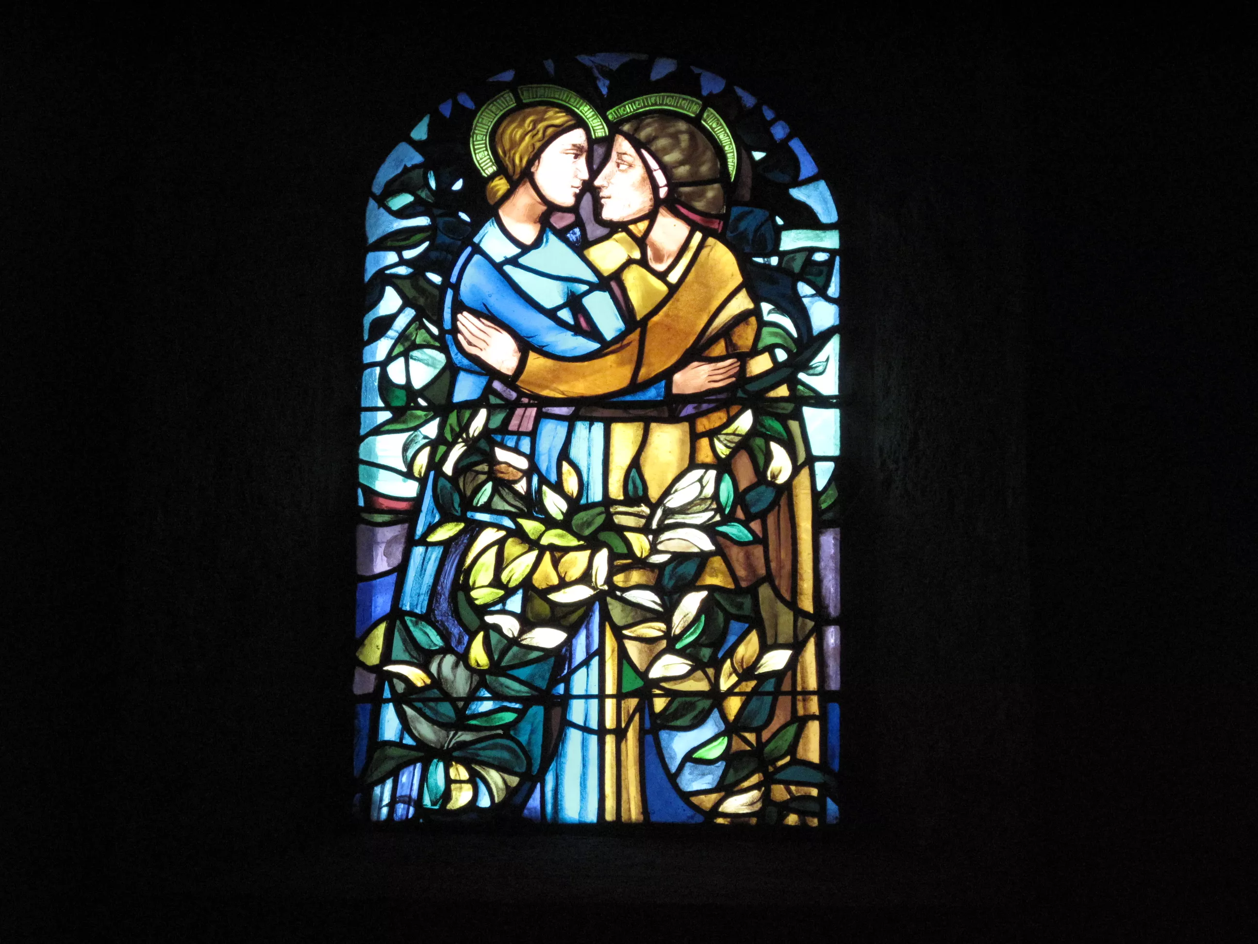 Marie vêtue de bleu, embrasse sa cousine Elisabeth vêtue de marron. Leurs têtes sont auréolées de vert et leurs corps sont entourés de feuilles