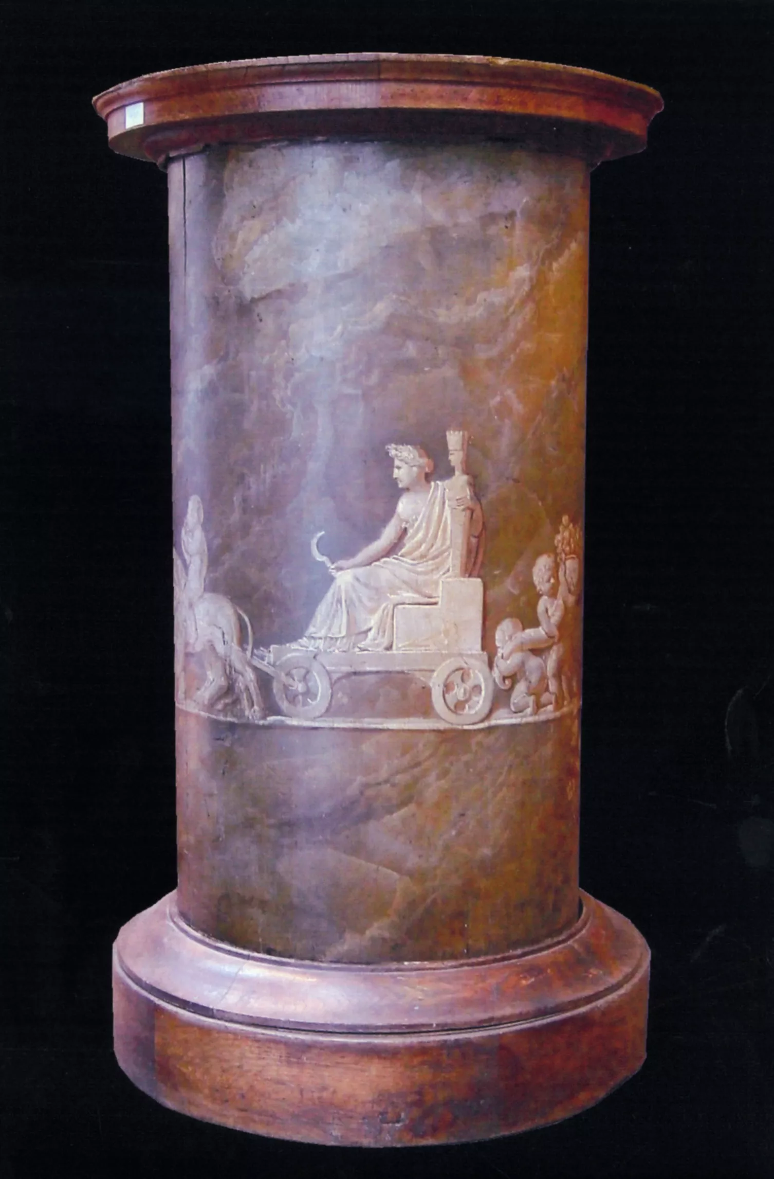 Photographie d'un piédestal avec une frise représentant un homme en toge assis sur une charrette tenant une faucille