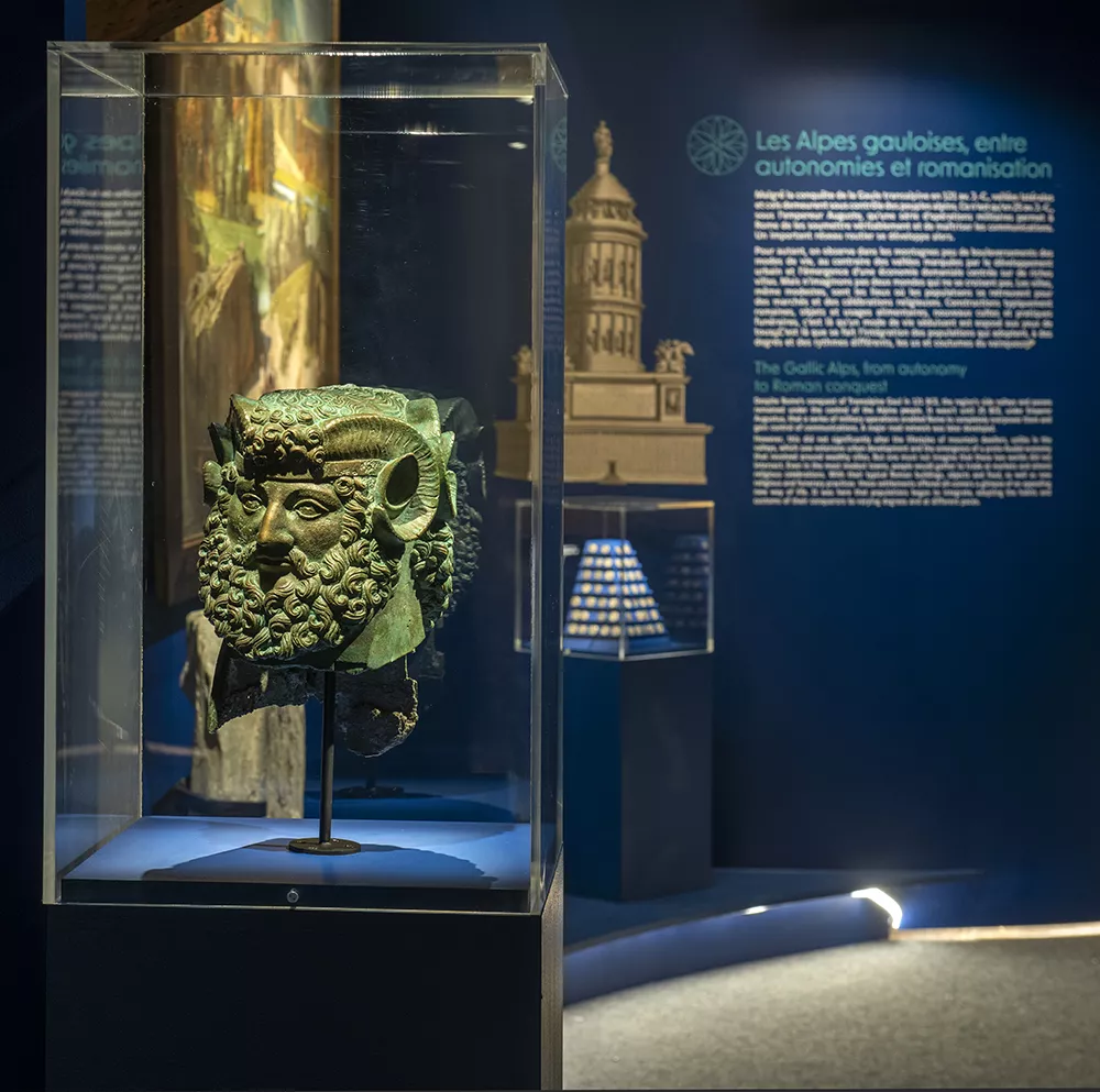 Photographie d'une salle de l'exposition &quot;Alpins&quot; présentant une sculpture du dieu Janus à deux visages