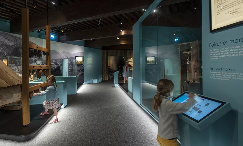 Photographie d'une salle de l'exposition &quot;Alpins&quot; montrant deux petites filles interagissant avec les dispositifs interactifs (écran et cloches pour animaux)