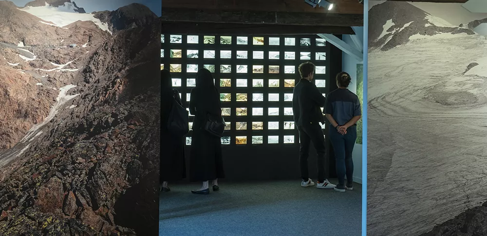 Photographie d'une salle de l'exposition &quot;Alpins&quot; présentant un mur d'anciennes cartes postales du territoire