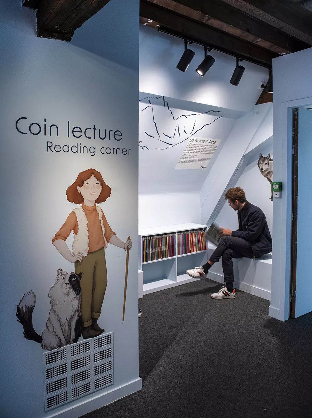 Photographie du coin lecture de l'exposition &quot;Alpins&quot; montrant un homme feuilletant les ouvrages en libre accès