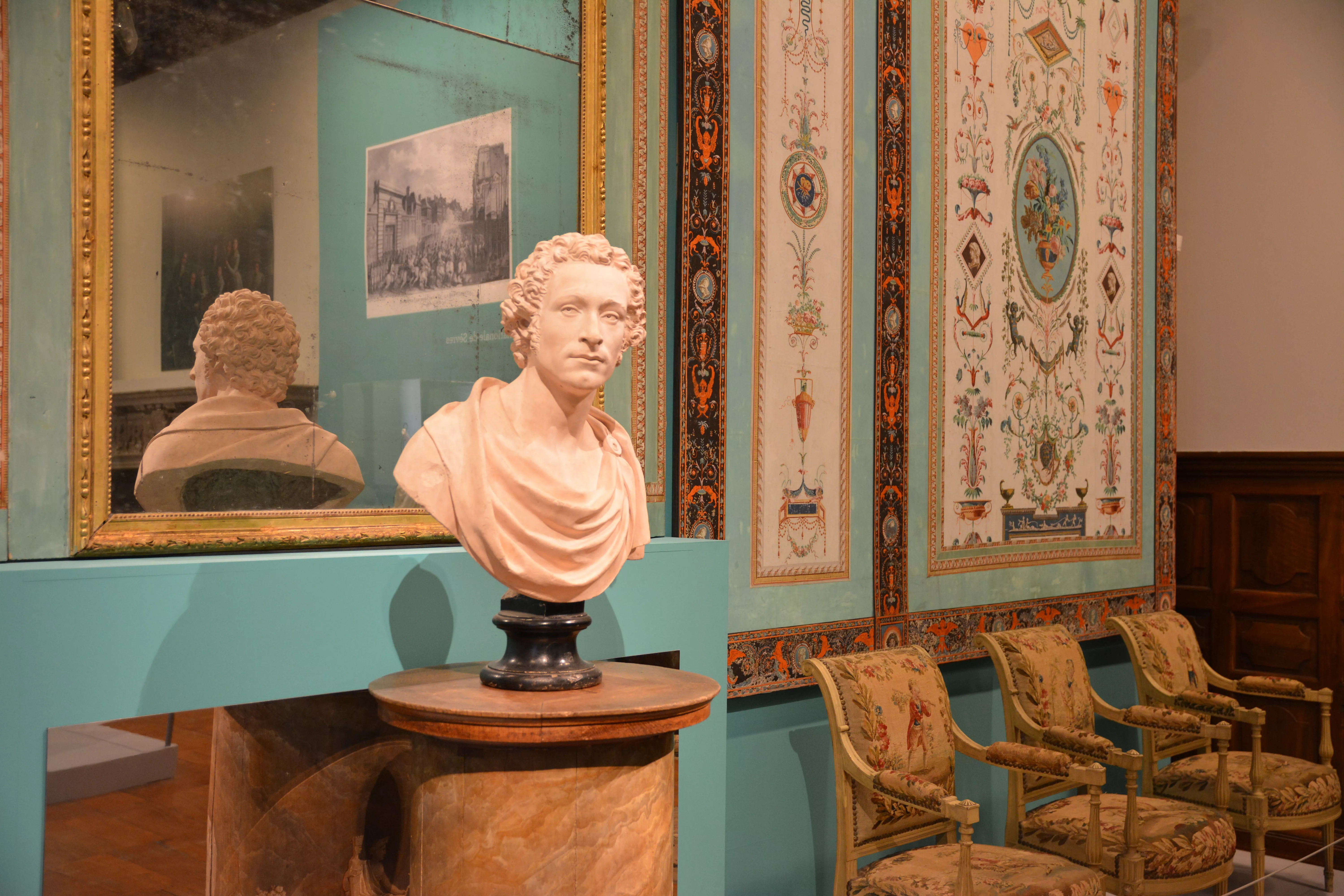 Photographie d'une salle de l'exposition &quot;Style Révolution française&quot; exposant un buste d'homme en marbre devant un mur présentant des papiers peints anciens
