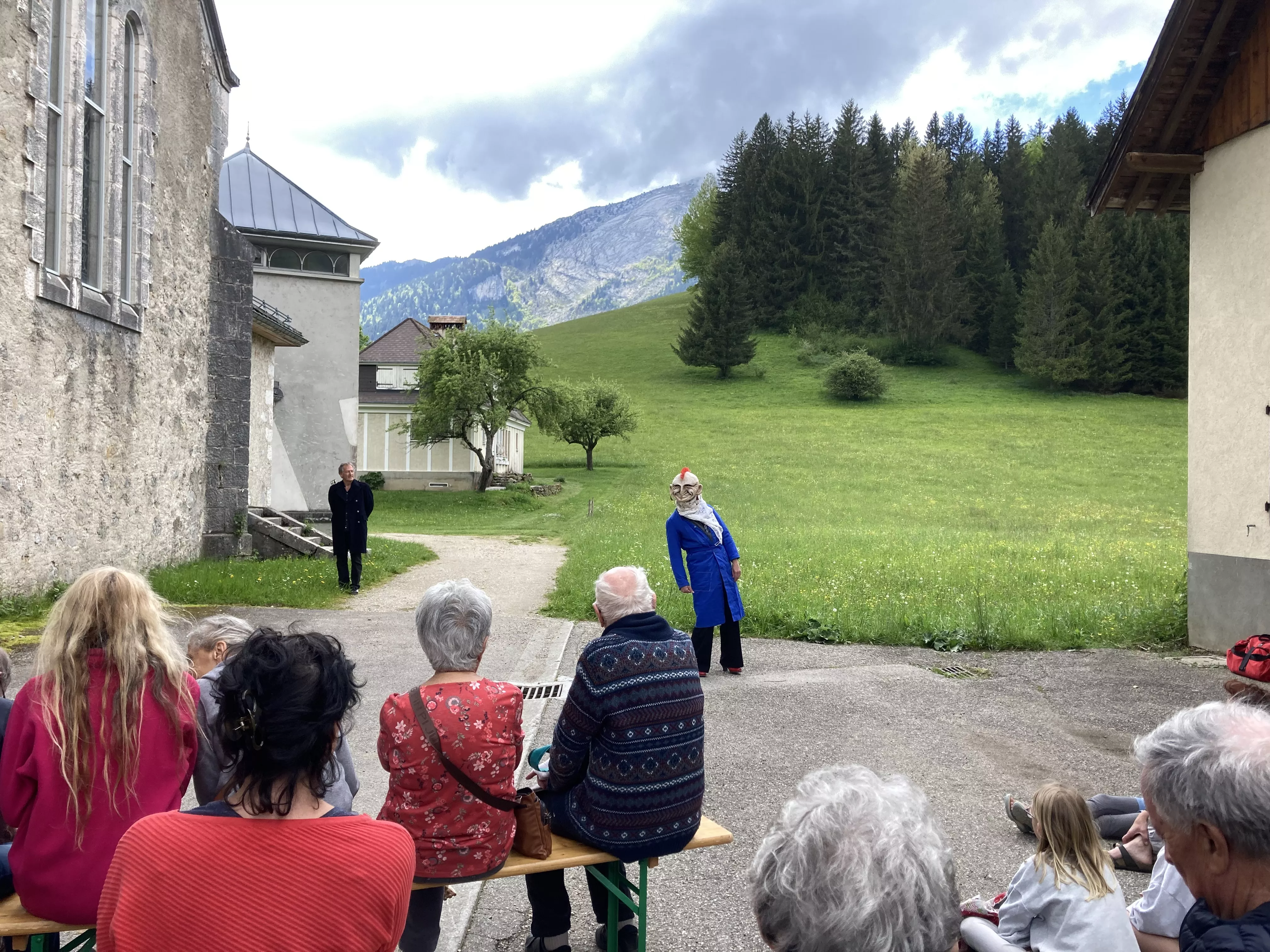Photographie de l'inauguration de l'exposition &quot;Text'îles&quot; en plein air montrant un membre du Turak Théâtre portant un masque souriant coiffé d'une crête orange