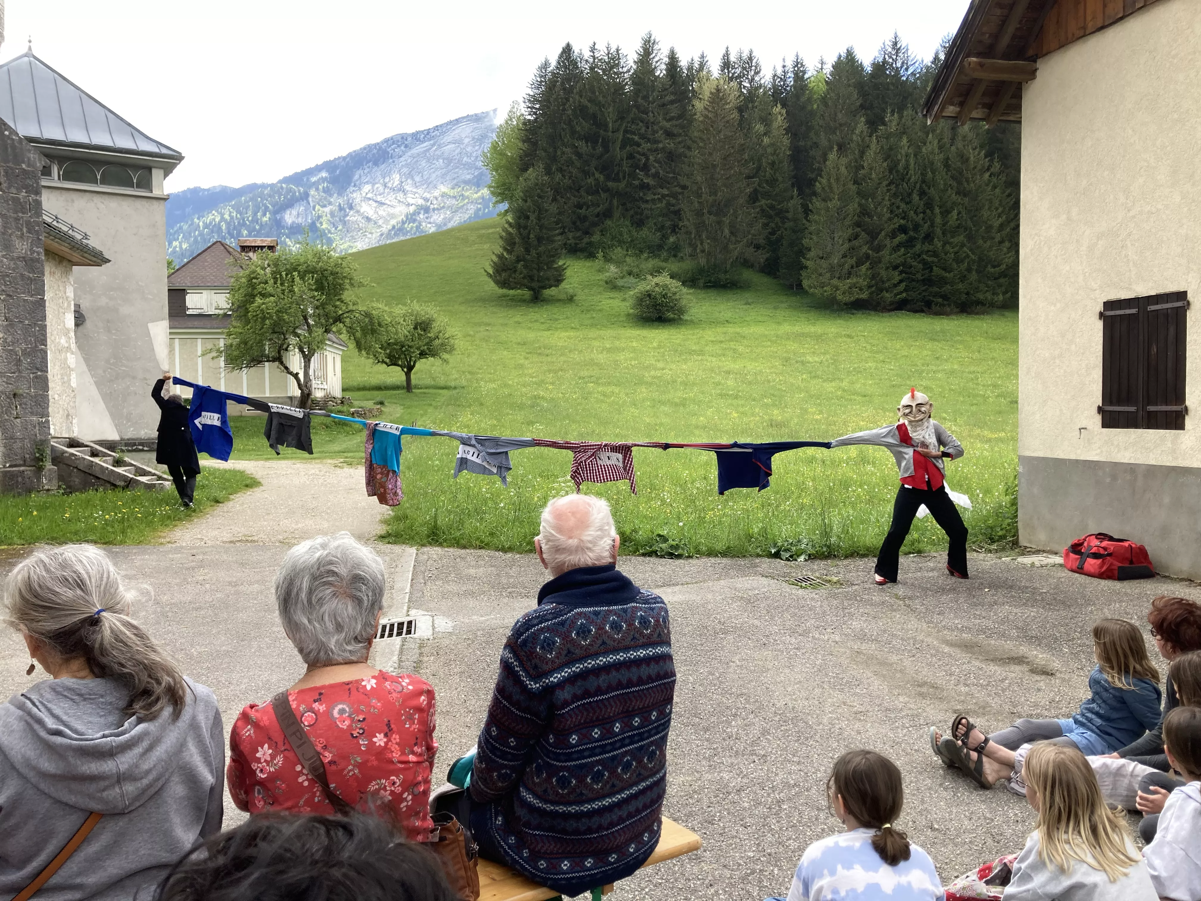 Photographie de l'inauguration de l'exposition &quot;Text'îles&quot; en plein air montrant deux membres du Turak Théâtre reliés par une chaîne de vêtements accrochés les uns aux autres