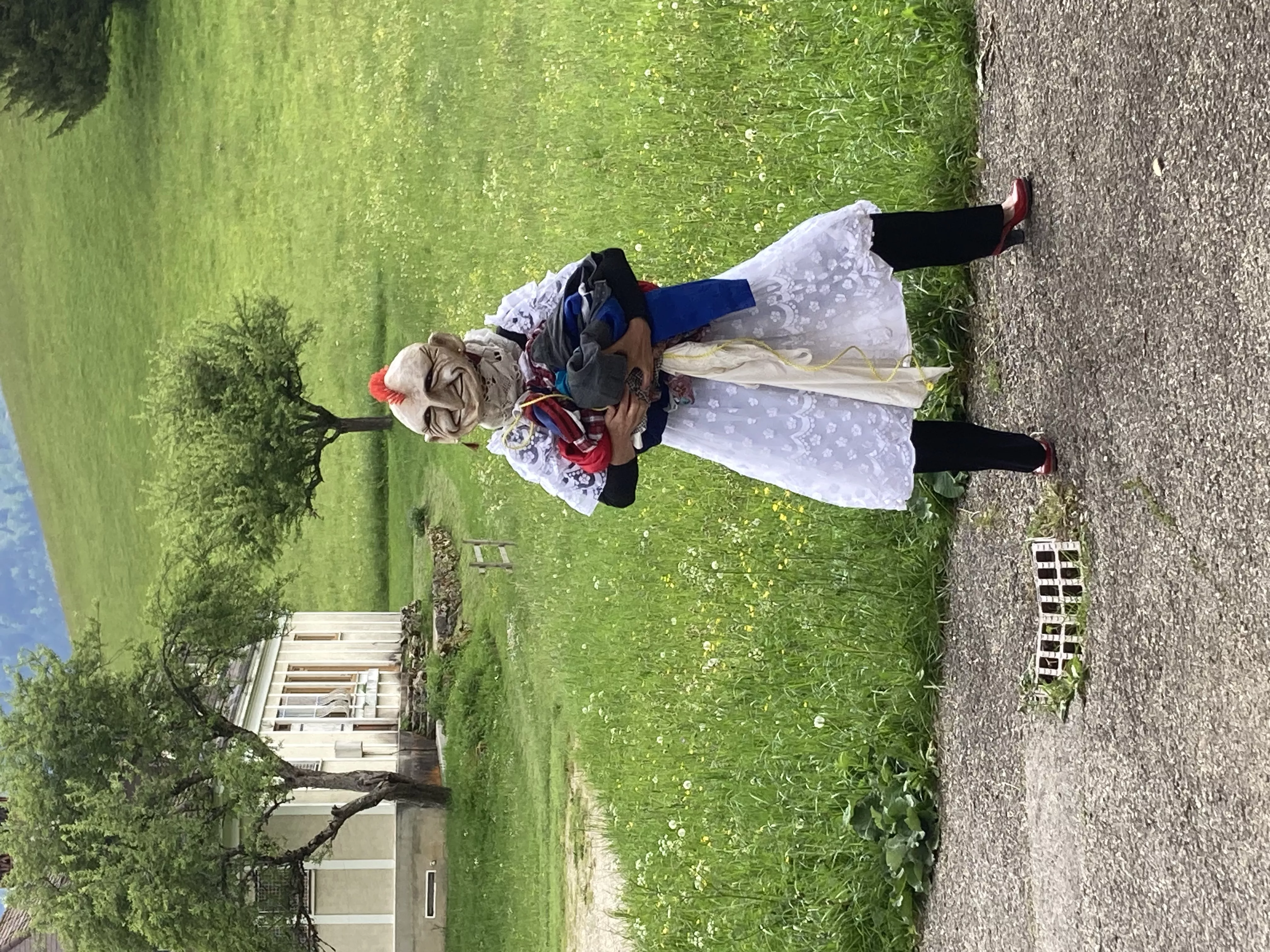 Photographie de l'inauguration de l'exposition &quot;Text'îles&quot; en plein air montrant un artiste du Turak Théâtre portant une pile de vêtements dont le visage est caché par un masque souriant