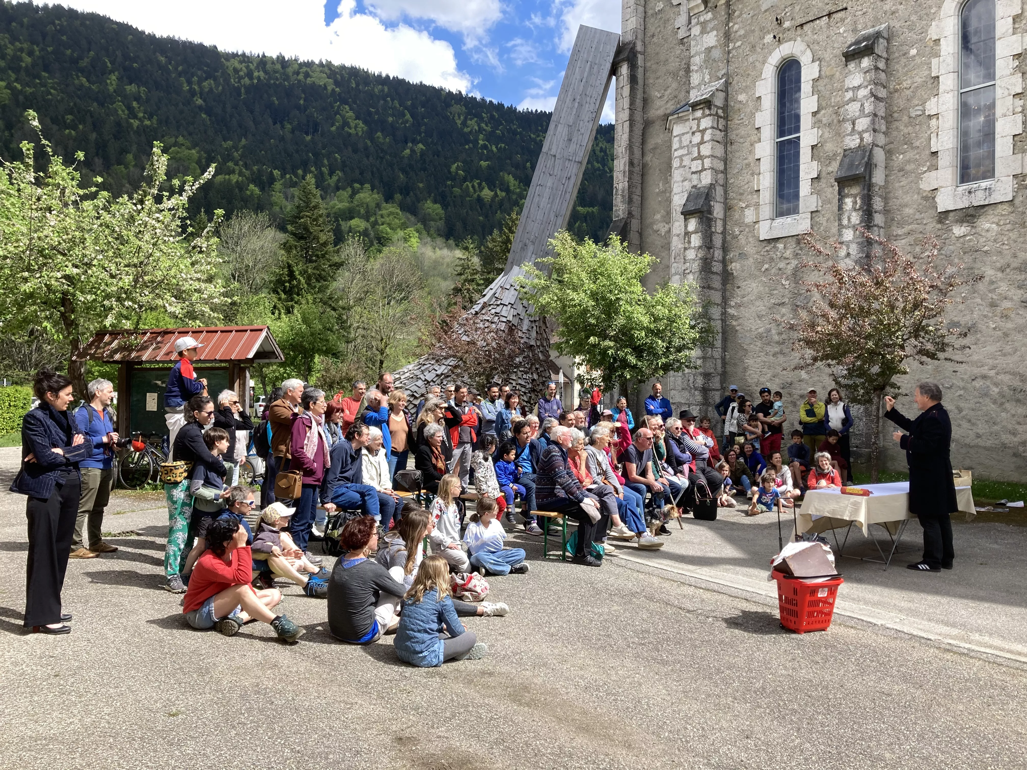Photographie de l'inauguration de l'exposition &quot;Text'îles&quot; avec le Turak Théâtre en plein air devant un public intergénérationnel le long de l'église d'Arcabas