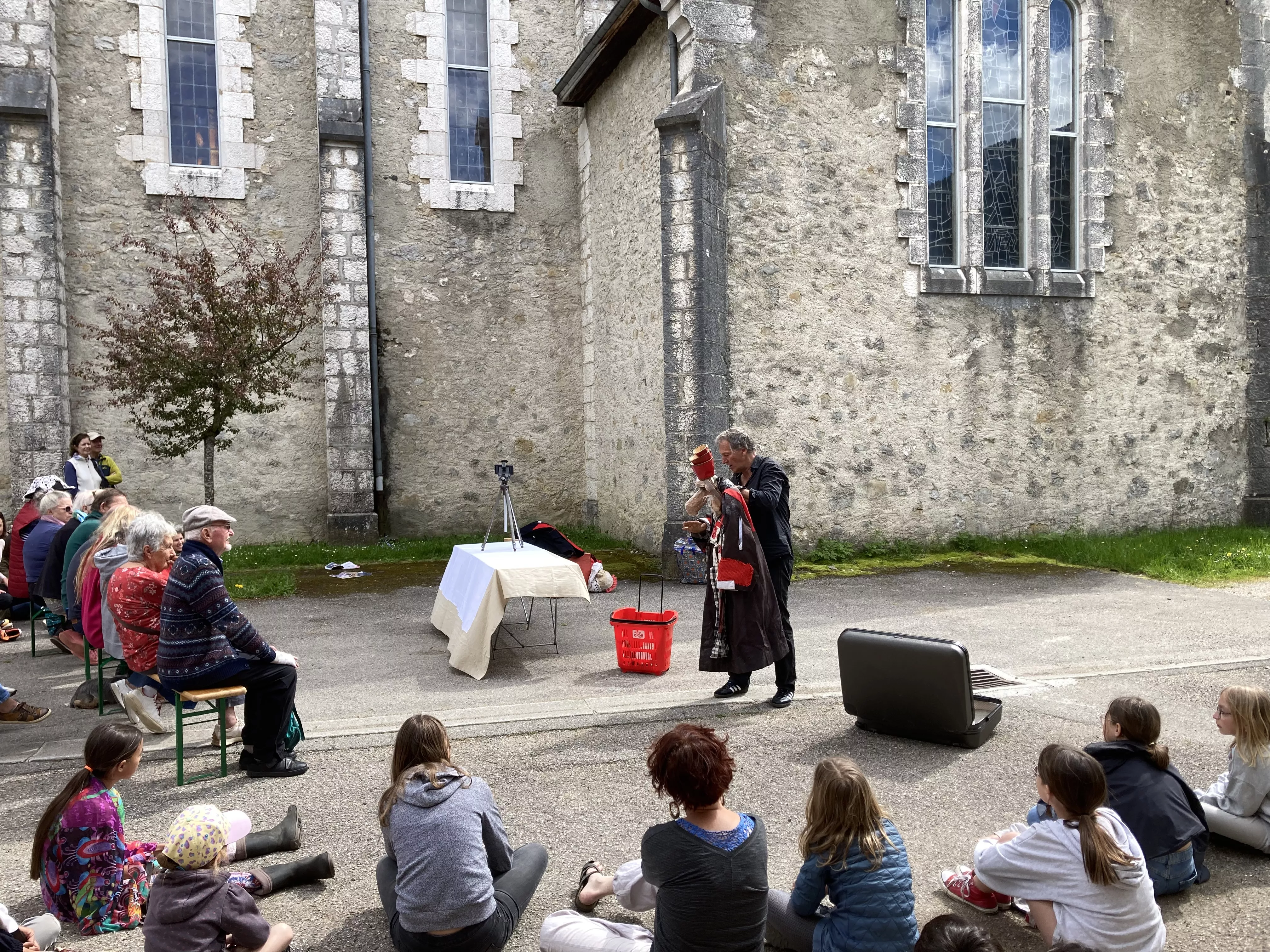 Photographie de l'inauguration de l'exposition &quot;Text'îles&quot; montrant un artiste du Turak Théâtre manipulant une marionnette devant un public intergénérationnel
