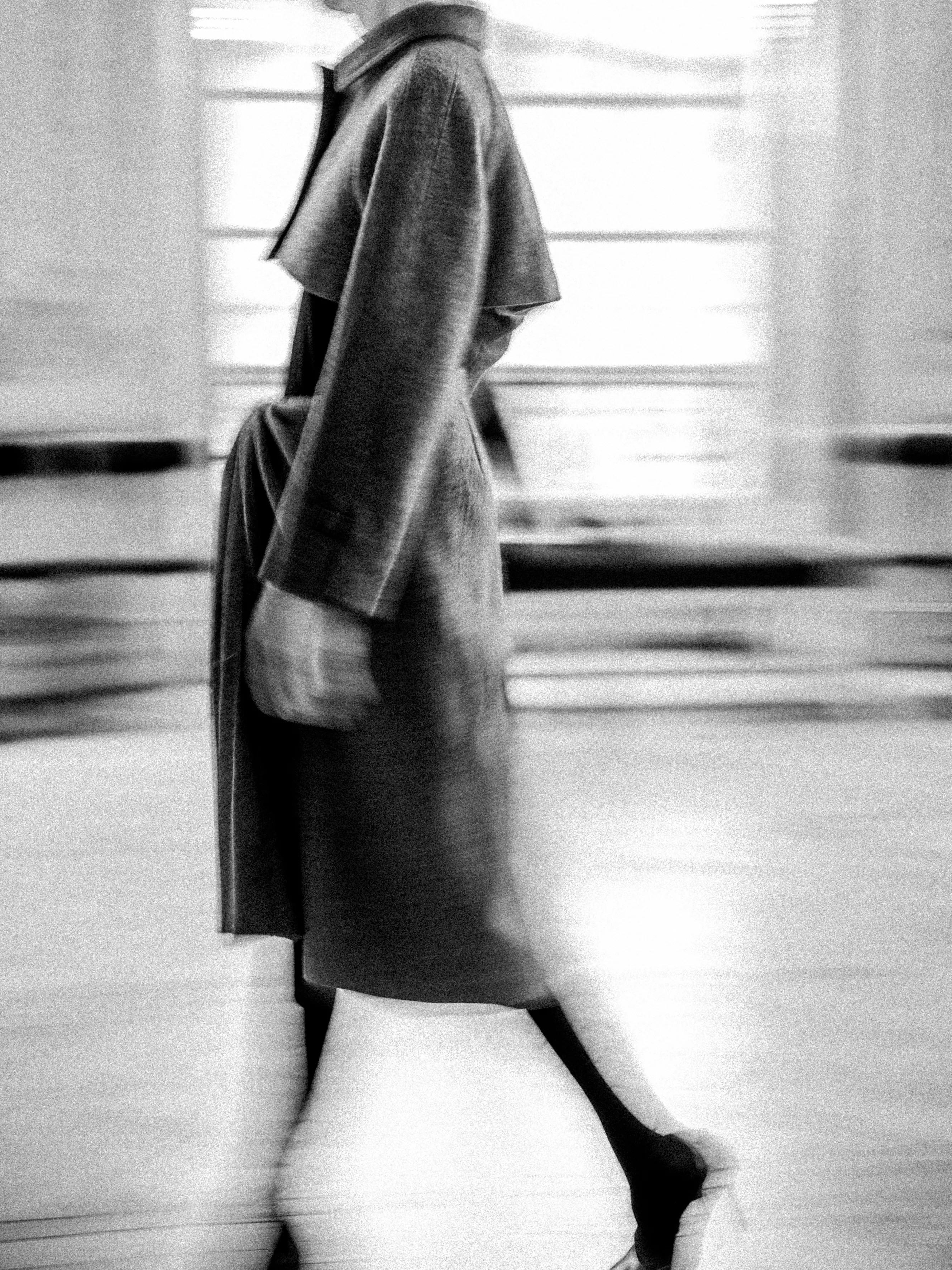Photo en noir et blanc : Femme avec un long manteau qui défile lors d'une performance d'Olivier Saillard