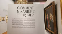 Photographie de l'exposition "Comment m'habillerai-je" au musée de la Révolution française montrant un texte explicatif sur un mur et un grand tableau sur la droite représentant un couple âgé