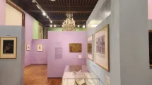 Photographie d'une salle de l'exposition "Comment m'habillerai-je" au musée de la Révolution française montrant des tableaux et des livres anciens dans une scénographie aux couleurs pastel (vert, violet et bleu)