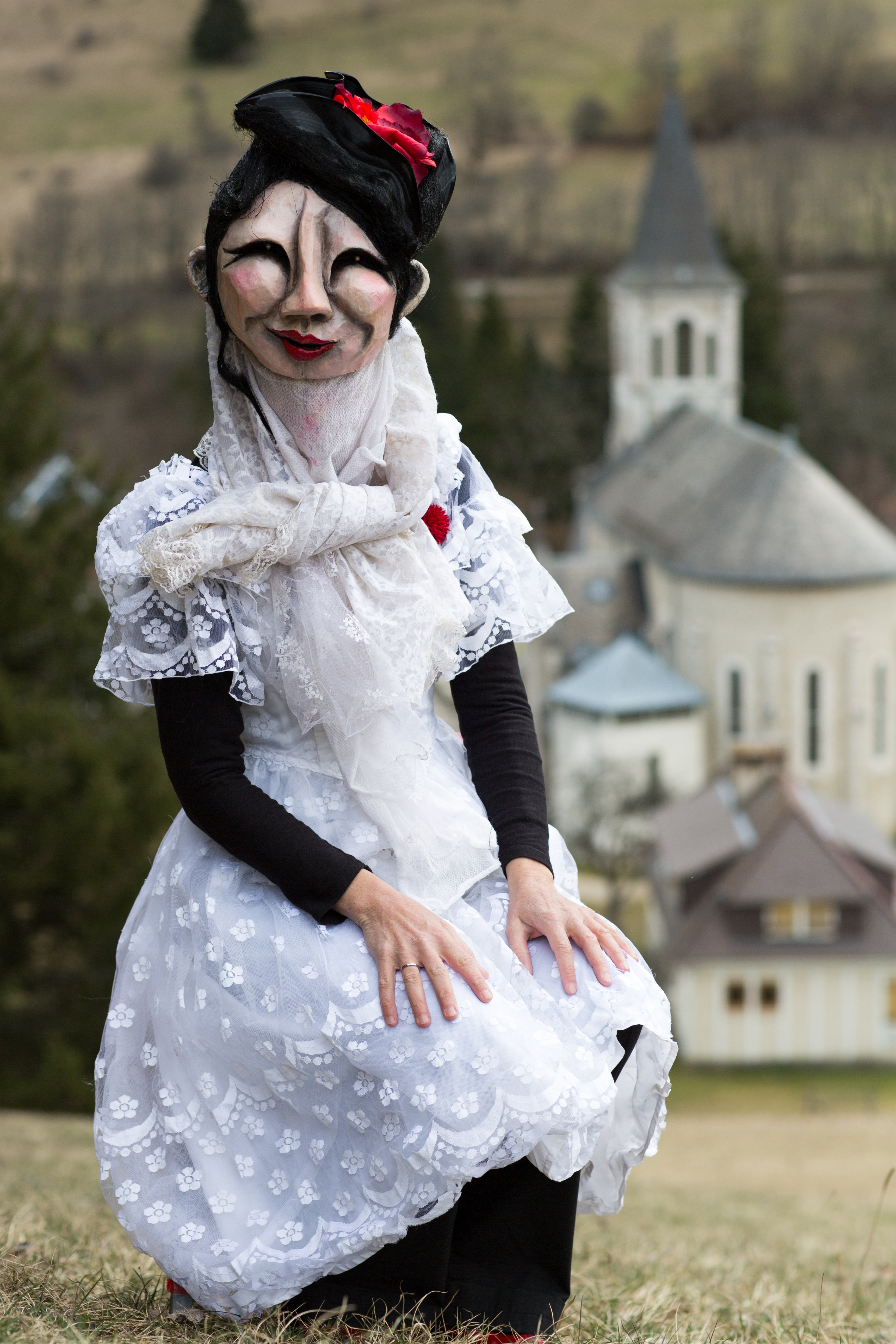 Photographie d'un personnage du Turak Théâtre masqué portant une robe de mariée devant l'église Saint Hugues © Raphael Licandro
