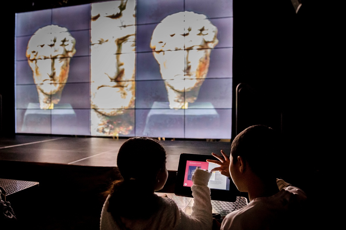 des enfants naviguent sur une tablette tactile pendant que des collections patrimoniales défilent sur l'écran de la micro folie © Jody Carter