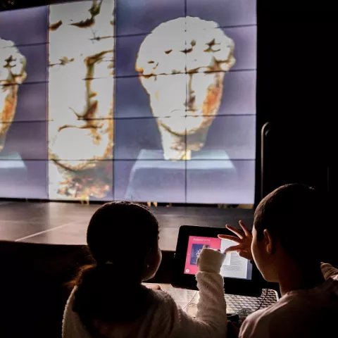 des enfants naviguent sur une tablette tactile pendant que des collections patrimoniales défilent sur l'écran de la micro folie © Jody Carter