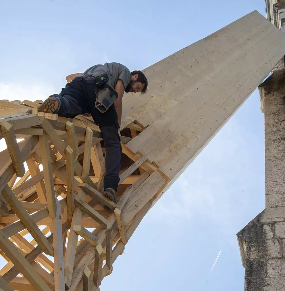 L'artiste Simon Augade assemble les chutes de bois en hauteur sur la structure de l'oeuvre "Fondement(s)" © Denis Vinçon pour le Département de l'Isère