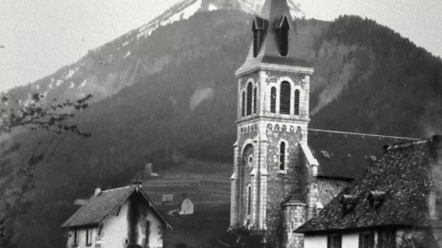 Vue sur l'église au 19ème siècle, photo en noir et blanc, deux hommes sur un chemin au premier plan. Derrière l'église, le Chamechaude.