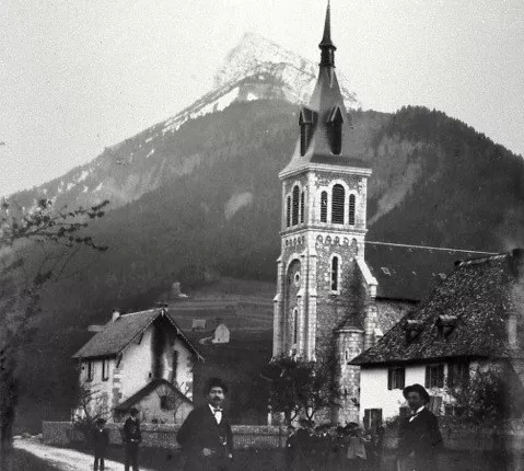 Vue sur l'église au 19ème siècle, photo en noir et blanc, deux hommes sur un chemin au premier plan. Derrière l'église, le Chamechaude.